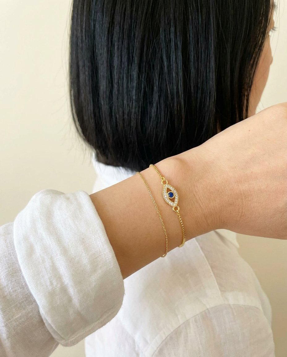 Aria Lucky Eye Bracelet stacked with a thin gold chain on white shirt